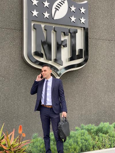 Christopher Gil in front of the NFL logo talking on a mobile phone holding a briefcase